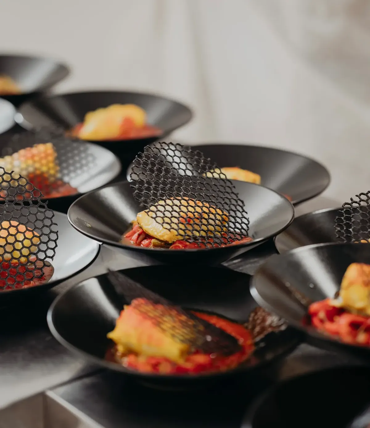 Black bowls plated at the pass with fish, tuile and pepper sauce.